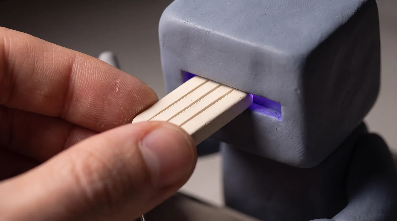 A hand slides an incised clay tablet into the slot in a robot’s head.